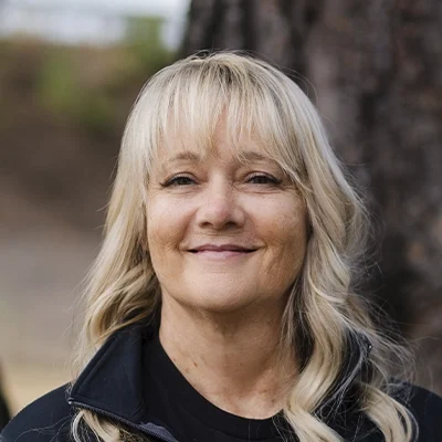 A headshot of Marilyn wearing a black shirt, photographed outdoors with a tree background.